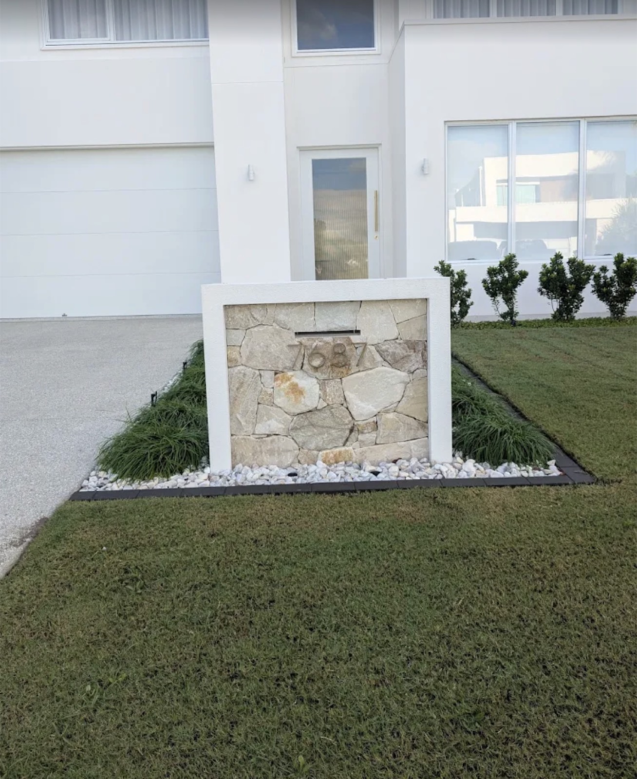 Stone letterbox entry feature with pebbles and fresh lawn