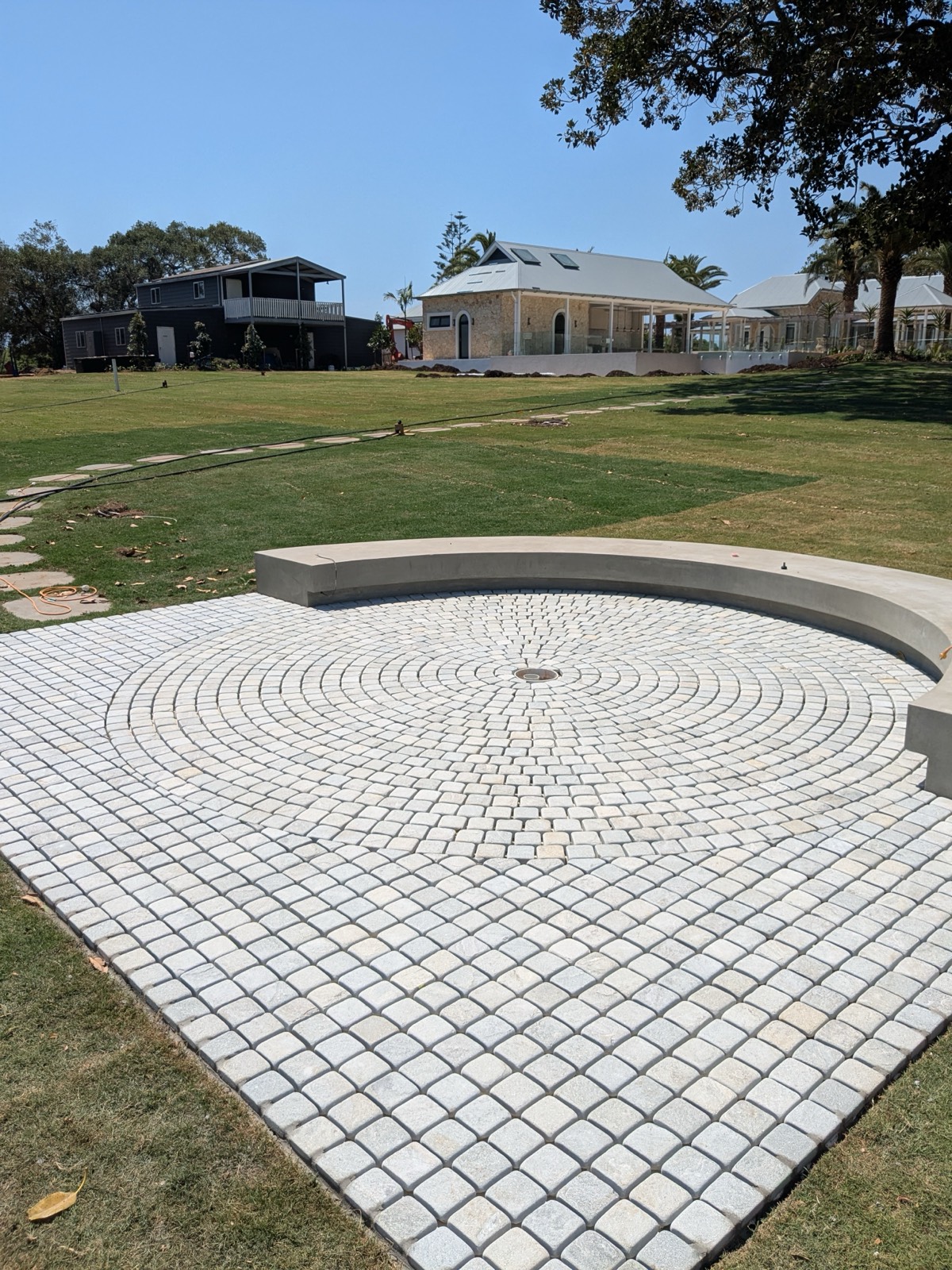 Circular cobblestone courtyard with curved concrete seat in a large lawn